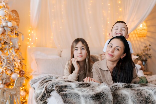 Mãe de família feliz e dois filhos deitados na cama à espera do Natal e rindo