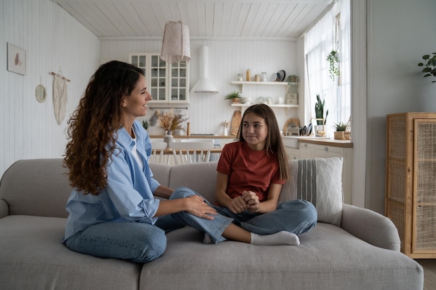 Mãe de família feliz e filha adolescente sentada no sofá conversando se divertindo em casa