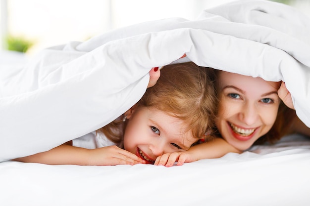 Mãe de família feliz e filha rindo na cama