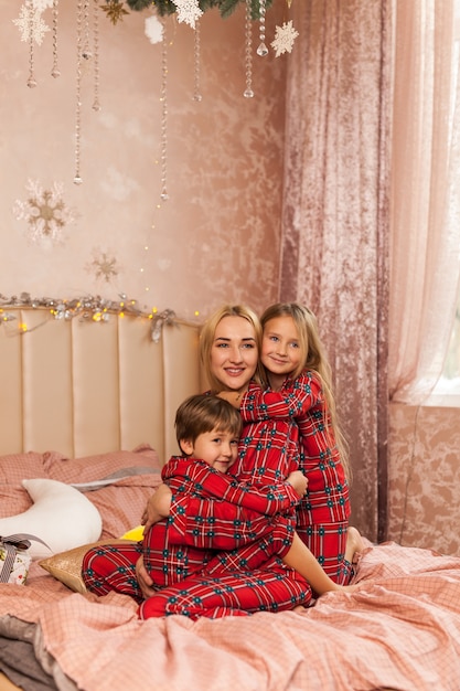 Mãe de família feliz e filhos na manhã de Natal na cama de pijama