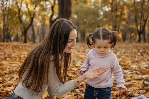 Mãe de família feliz e menina brincando ao ar livre no parque de outono, menina e sua mãe no