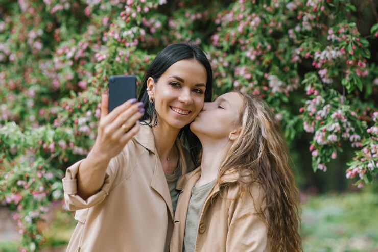 Mãe de família feliz e sua adorável filha adolescente na primavera no parque selfie com um smartphone