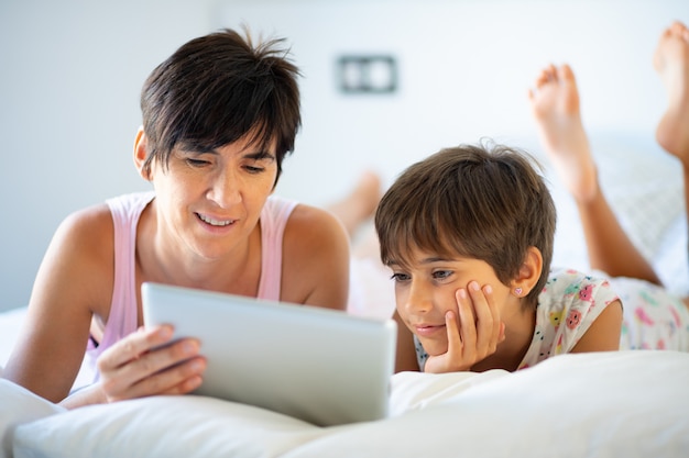 Mãe de meia-idade com sua filha de oito anos usando tablet digital no quarto.