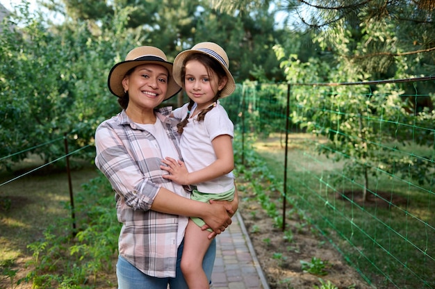 Mãe de mulher alegre segurando sua filha nos braços juntos em fileiras de mudas na fazenda orgânica