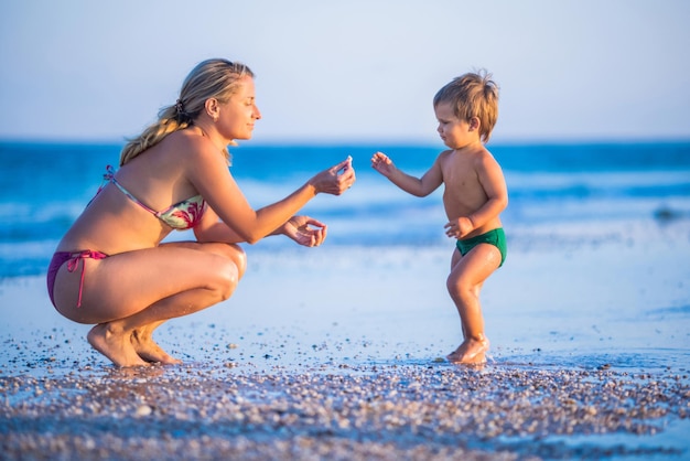Mãe de óculos brinca com uma criança sentada na praia perto do mar