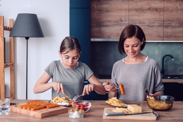 Mãe de pé junto à mesa em casa e servindo batatas fritas