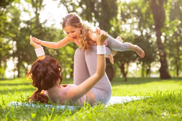 Mãe deitada no tapete no parque e segurando sua filha nas pernas no ar