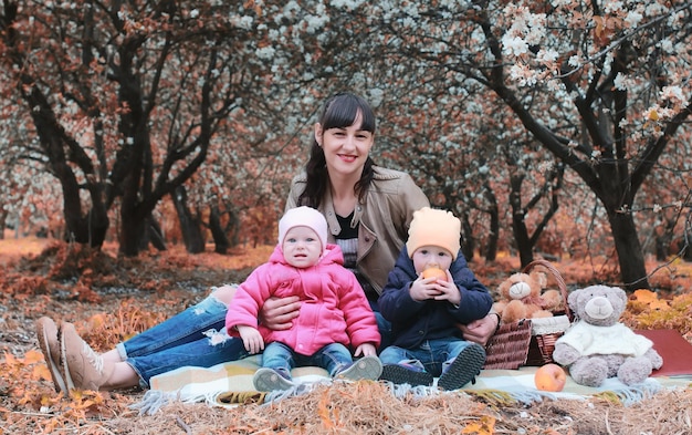 Mãe do parque outono com gêmeos na manta ao ar livre no jardim de maçã