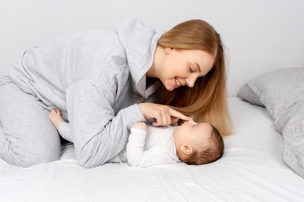 Mãe e bebê brincam na cama mãe e filho família feliz linda loira e bebê fofo em casa