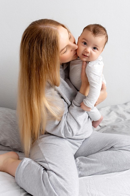 Mãe e bebê brincam na cama mãe e filho família feliz linda loira e bebê fofo em casa