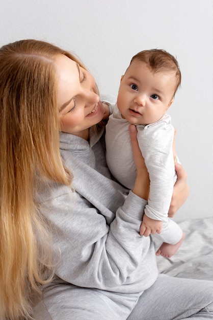 Mãe e bebê brincam na cama mãe e filho família feliz linda loira e bebê fofo em casa