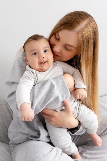 Mãe e bebê brincam na cama mãe e filho família feliz linda loira e bebê fofo em casa