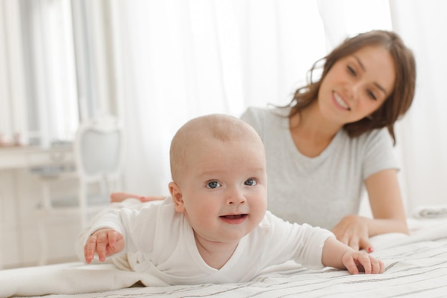 Mãe e bebê brincando e sorrindo na cama de família feliz. Menino olhando para a câmera