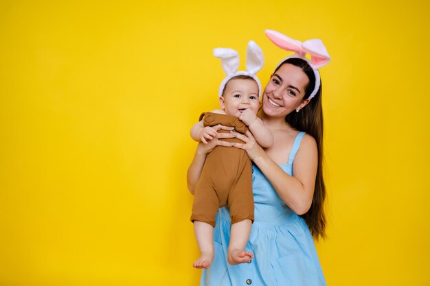 Mãe e bebê com orelhas de coelho Pai e filho brincam em fundo amarelo Família celebrando a Páscoa