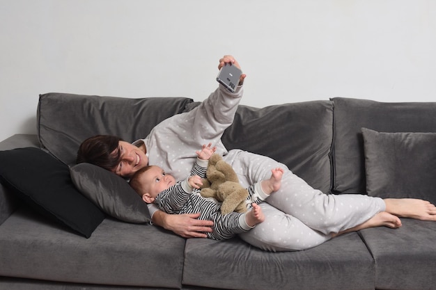 Mãe e bebê deitados no sofá fazendo uma selfie