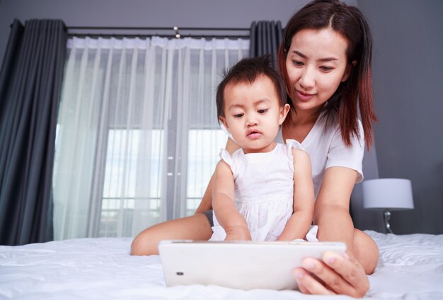 Mãe e bebê estão olhando para jogar e ler o computador tablet na cama