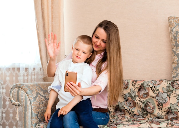 Mãe e bebê tirando uma selfie em uma aconchegante sala de estar. mãe e filho fazem caretas engraçadas e tiram fotos de si mesmos na câmera