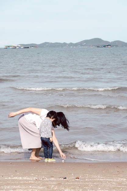 Mãe e criança asiática de 3 anos caminhando na praia.