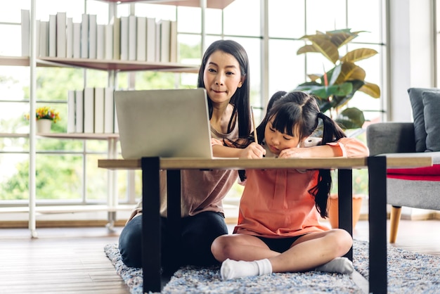 Mãe e criança asiática, menina, aprendendo e olhando para o laptop, fazendo lição de casa, estudando conhecimento com sistema de e-learning de educação online