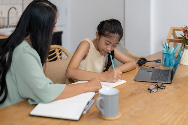 Mãe e criança asiática menina aprendendo on-line no computador portátil fazendo lição de casa estudando conhecimento com sistema de e-learning de educação on-line crianças videoconferência com professor tutor em casa