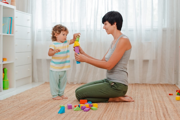 Mãe e criança brincam no chão no berçário. mãe e um menino estão construindo uma torre de blocos coloridos.