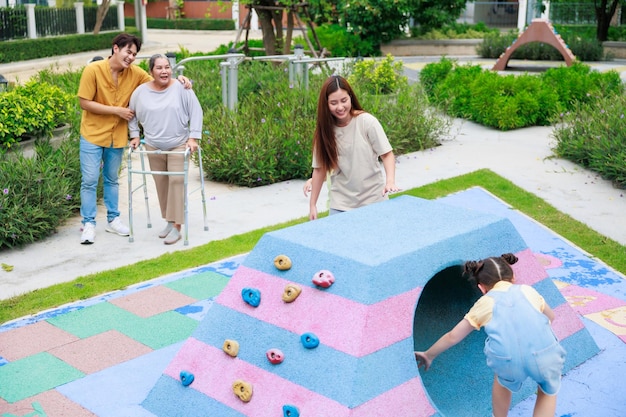 Mãe e dois filhos se divertem correndo juntos enquanto pai e avó procurando por eles brincam no playground