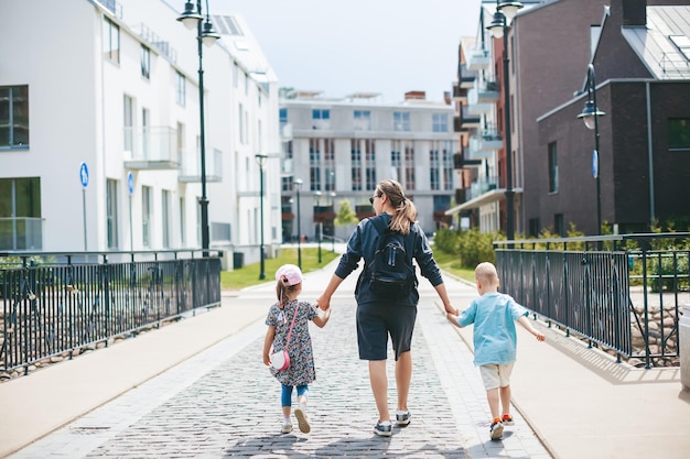 Mãe e dois filhos, um menino e uma menina andando de mãos dadas pela cidade