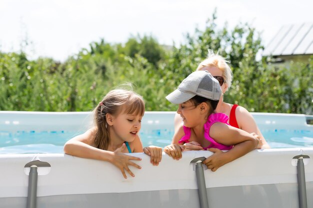 Mãe e duas filhas brincando na água da piscina mulher e duas meninas se divertem na piscina em casa espirrando água e sorrindo