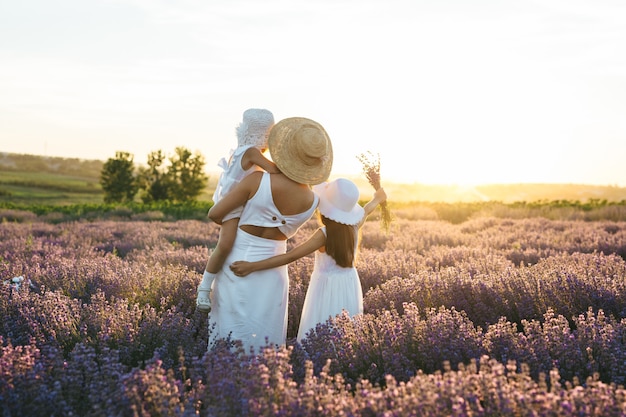 Mãe e duas meninas olham para o pôr do sol no campo de lavanda