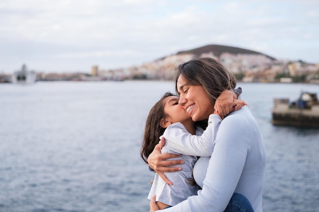 Mãe e filha abraçadas à beira-mar ao pôr do sol ao ar livre Conceito Estilo de vida amor cuidado da família