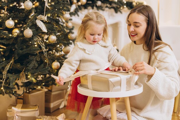 Mãe e filha abrindo presente de Natal por árvore decorada