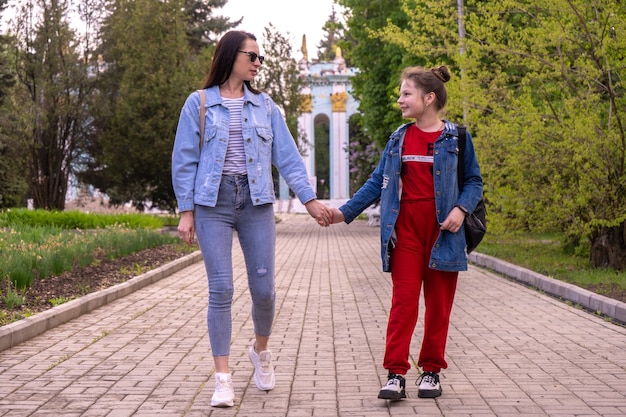 Mãe e filha adolescente caminhando em um parque, de mãos dadas, uma jovem feliz mulher caucasiana com cabelo comprido e uma adolescente andando em uma cidade, estilo de vida familiar