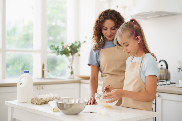 Mãe e filha adolescente fazendo massa para pastelaria juntas na cozinha