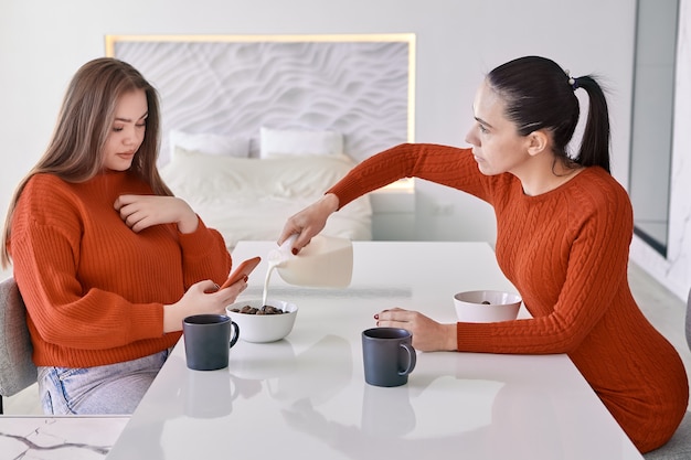 Mãe e filha adulta, vestidas de vermelho, comem cereal matinal com leite.