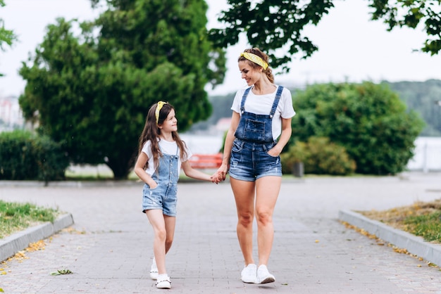 Mãe e filha andando segurando mão em mão e olhando um ao outro ao ar livre.