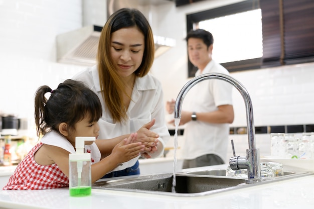 Mãe e filha asiática lavando as mãos com sabão na pia de uma cozinha