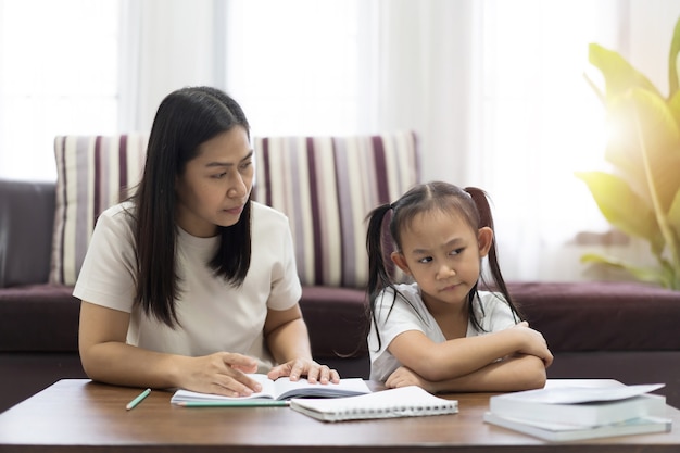 Mãe e filha asiáticas cansadas e entediadas ensinando lição de casa, conceito de ideia de trabalho entediante study from home