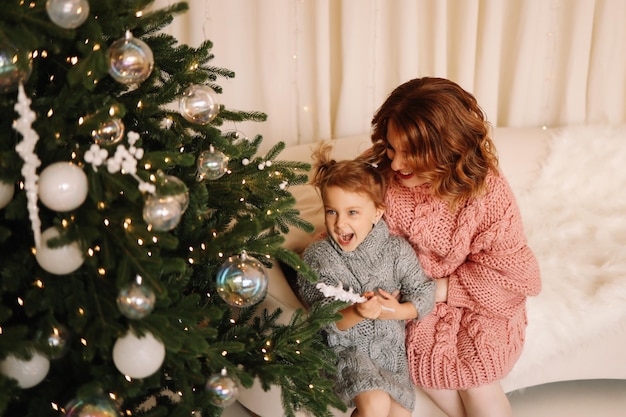 Mãe e filha bebê em camisolas abraçando-se preparando-se para as férias de Natal em casa