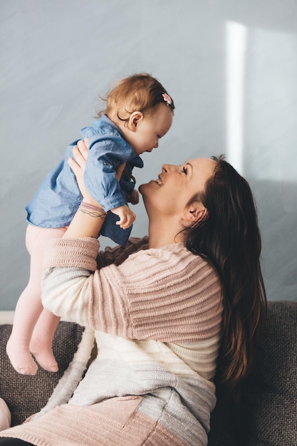 Mãe e filha bebê se divertindo no sofá em casa Família feliz