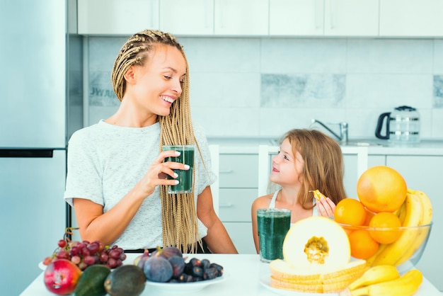 Mãe e filha bebendo smoothie verde em uma cozinha branca família mãe e filho filha blen