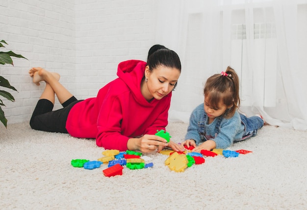 Mãe e filha brincam de construtor no tapete da sala. família feliz