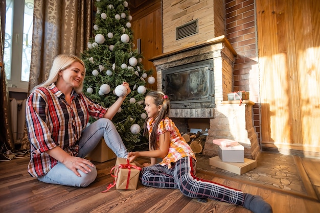 Mãe e filha brincando com bolas perto da árvore de Natal. presentes, luzes, bolas de fundo.