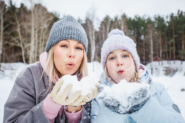 Mãe e filha brincando com neve, soprando neve das palmas das mãos, caminhada de inverno