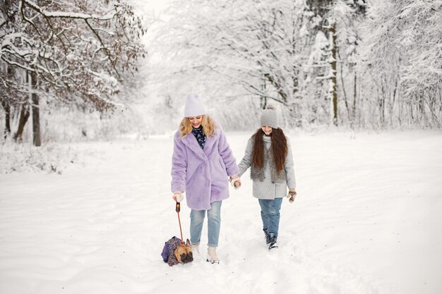 Mãe e filha brincando com seu cachorro bulldog francês na neve