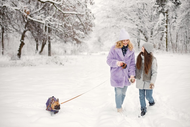 Mãe e filha brincando com seu cachorro bulldog francês na neve