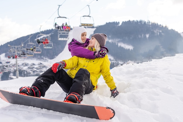 Mãe e filha brincando na neve com pranchas de snowboard