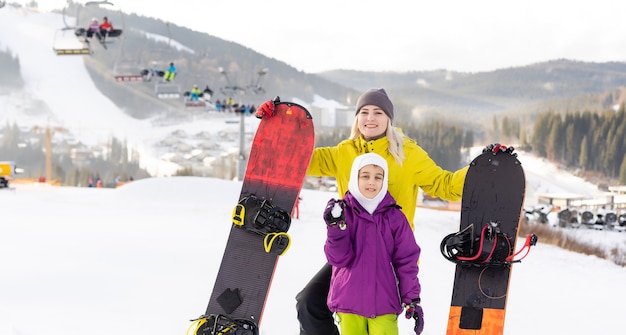 Mãe e filha brincando na neve com pranchas de snowboard