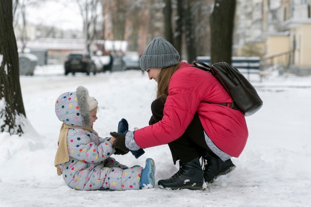 Mãe e filha caminham lá fora no inverno e desfrutam da primeira neve.