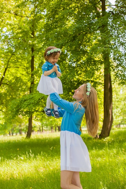 Mãe e filha caminham pela floresta com as mesmas roupas e tiaras. Filha nos braços da mãe