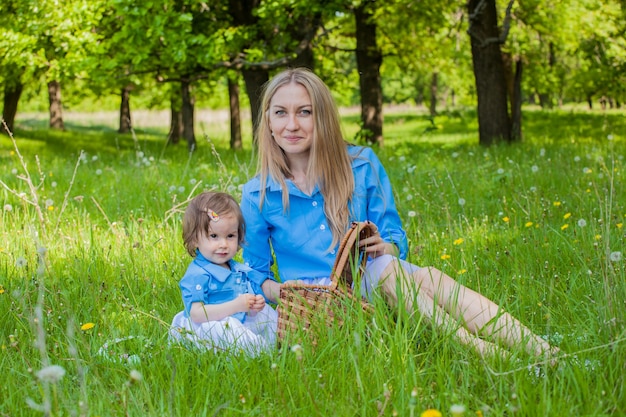 Mãe e filha caminham pela floresta com as mesmas roupas e tiaras. Piquenique